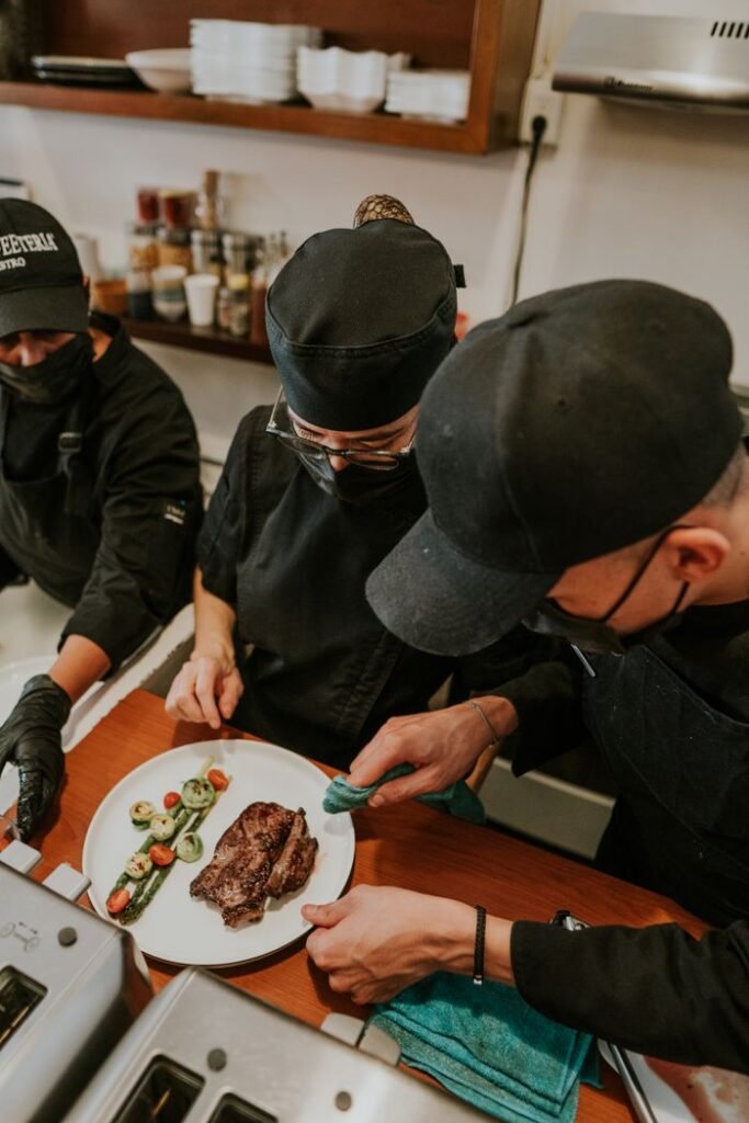 Team of chefs focused on plating a gourmet steak dish in a professional kitchen setting.